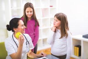 Female registered dietitians talks with teenagers while holding apple.
